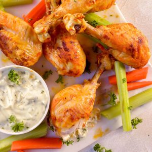 buffalo drumsticks, celery, carrots and blue cheese dip on white plate