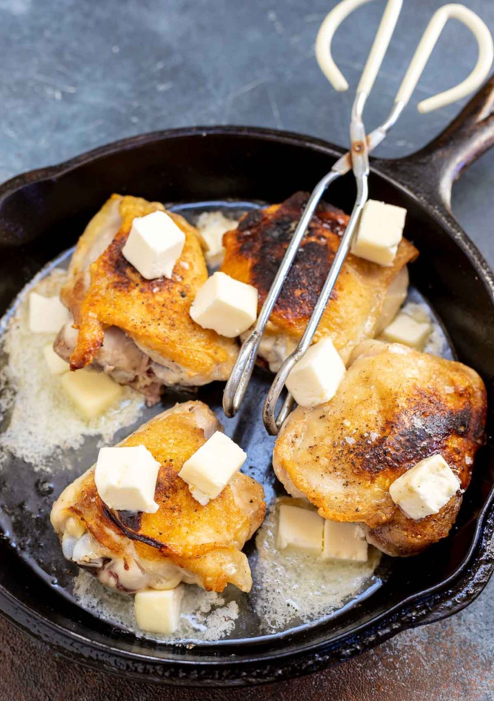 browned chicken thighs topped with cubed butter in black cast-iron pan