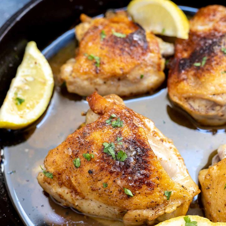 browned chicken thighs with lemon wedges in black pan