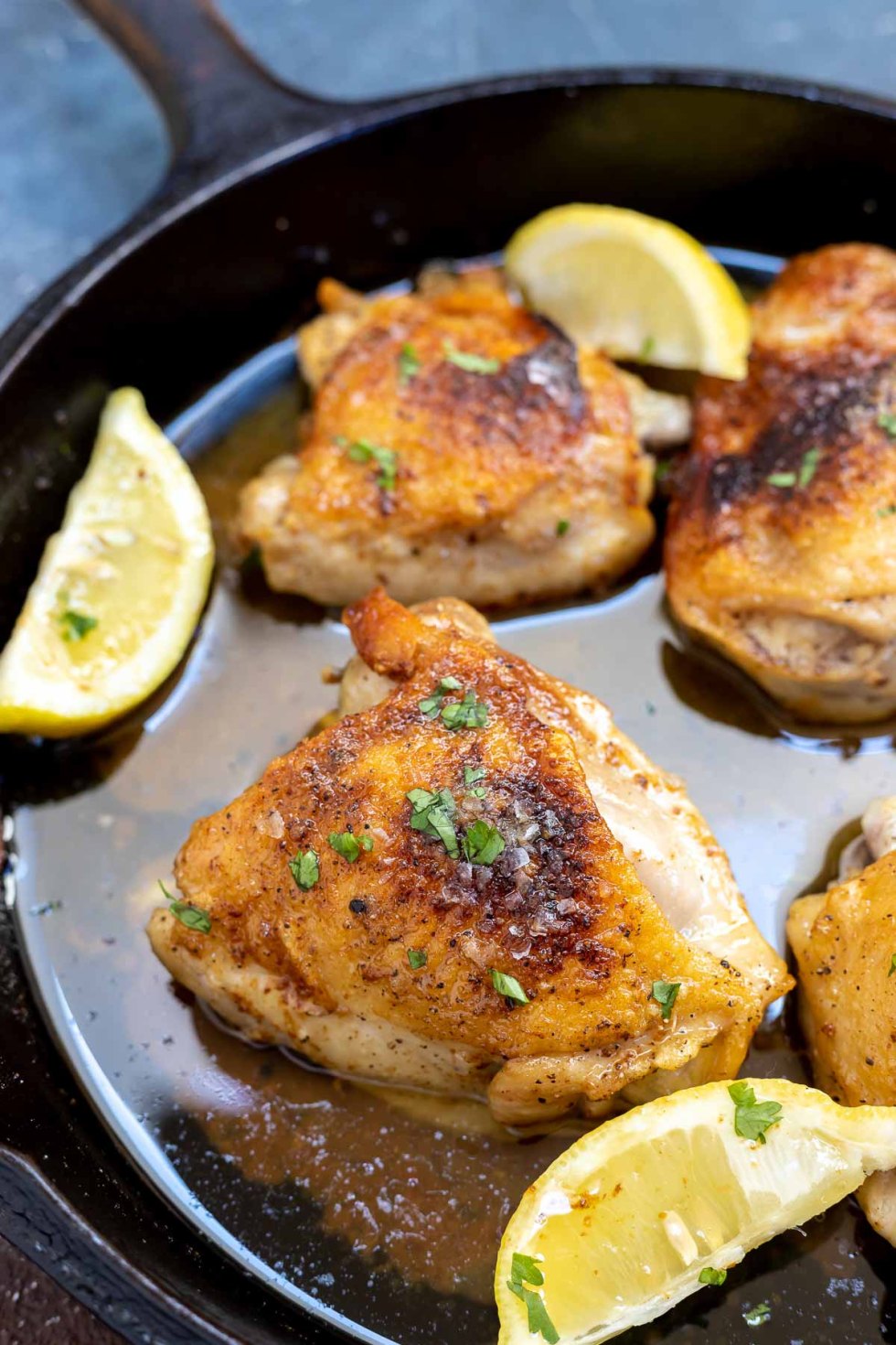 browned chicken thighs with lemon wedges in black pan 