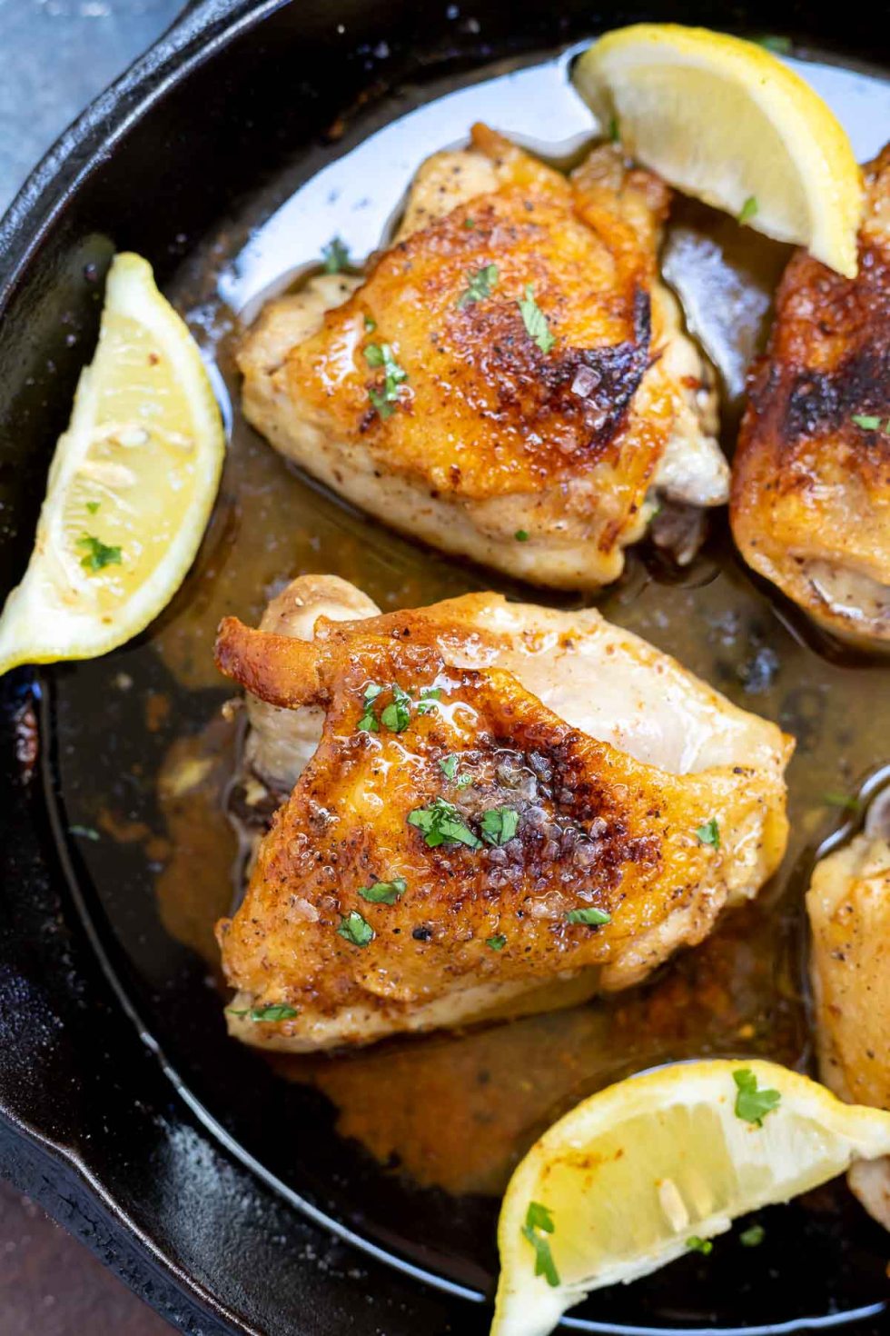 crisp brown chicken thighs and lemon wedges in black cast iron pan