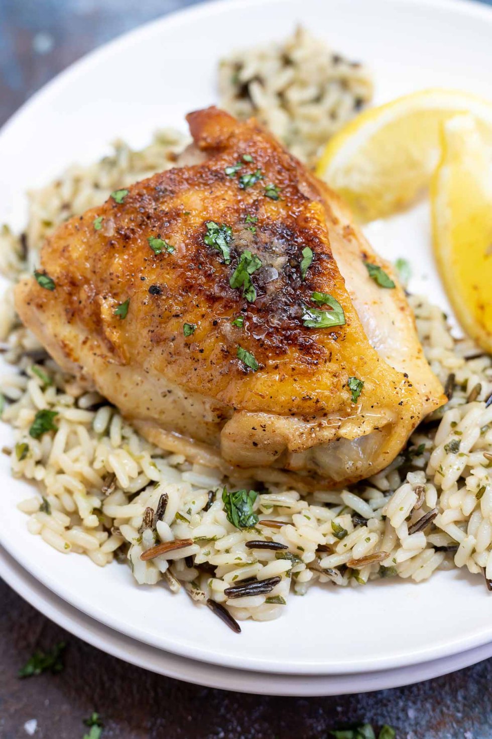 browned chicken thigh, wild rice and lemon wedges served on white plate