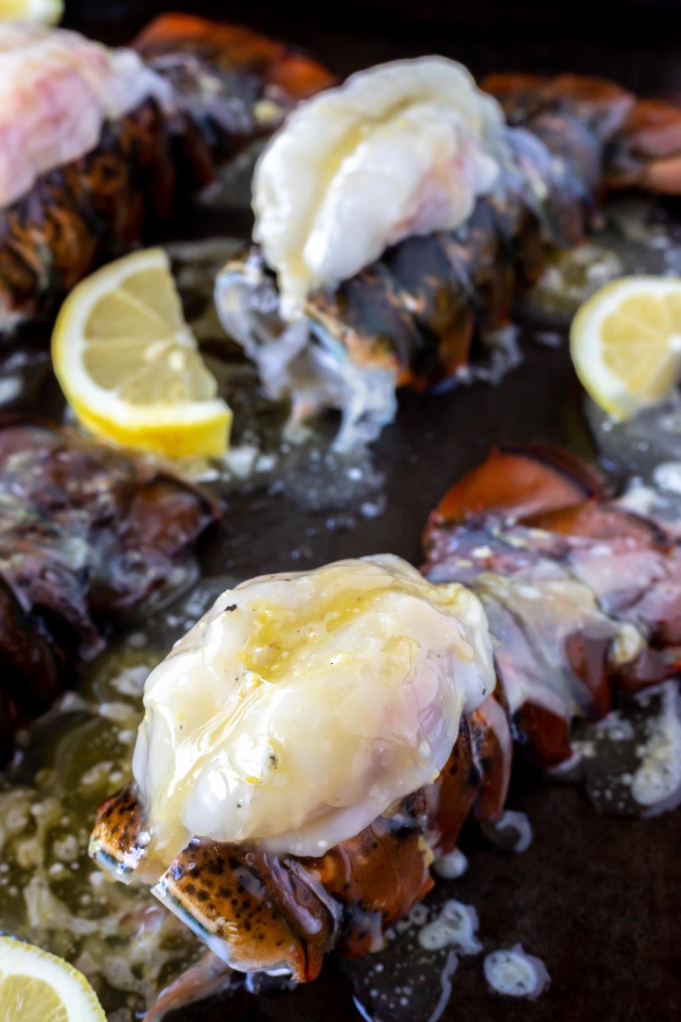 prepped buttery lobster and lemons on rimmed baking sheet