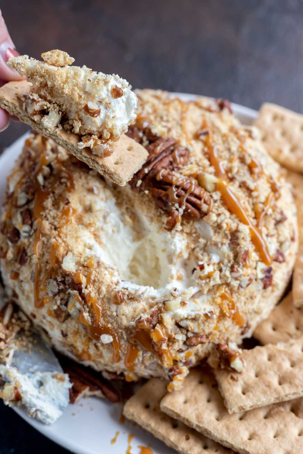 sweet cheeseball and hand holding graham cracker topped with creamy spread