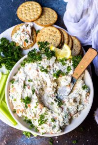 cold crab dip in white bowl with metal spreading knife