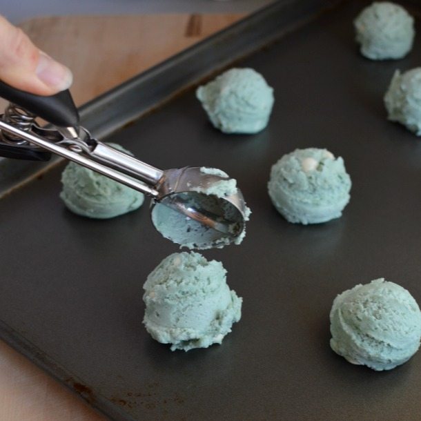 cookie dough balls on baking sheet with hand holding scooper