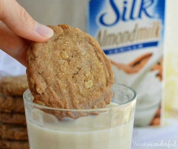 hand dipping cookie into glass of almond milk