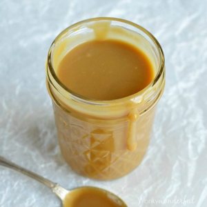 clear jar filled with caramel next to spoon