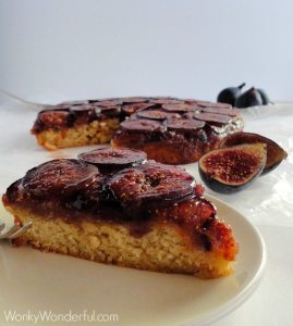 slice of fig cake on white plate with figs and cake in the background