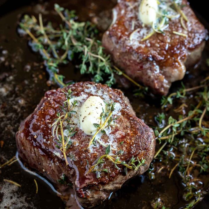 two butter herb topped filet mignon in cast iron pan