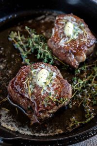 two butter herb topped filet mignon in cast iron pan