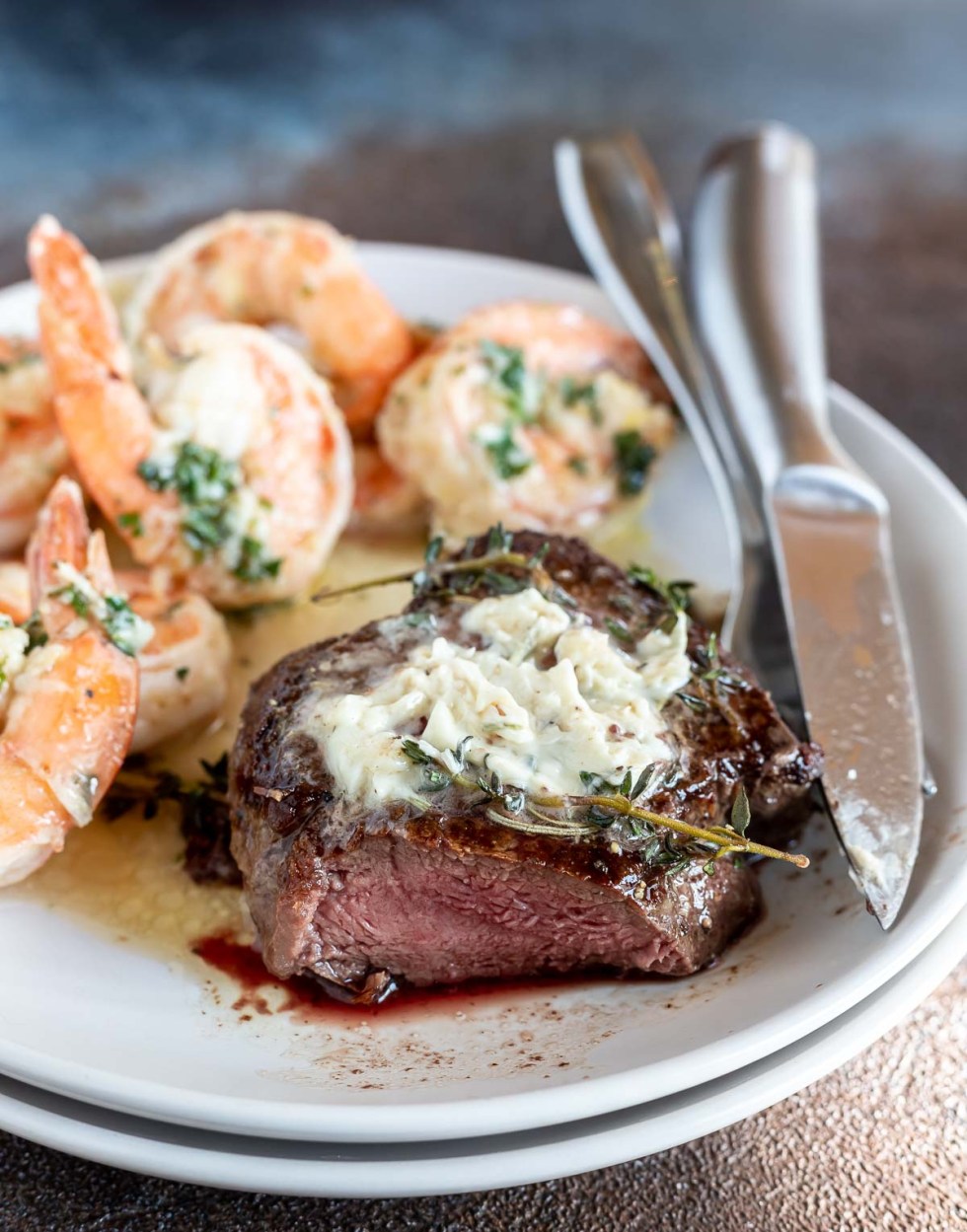 butter topped steak with slice cut out served next to shrimp on white plate