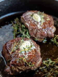 two cooked filet mignon steaks topped with butter and thyme in pan