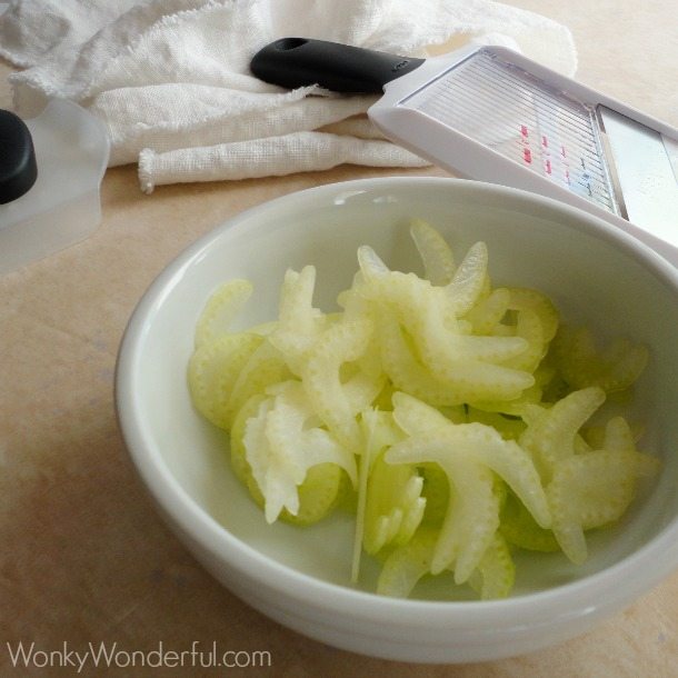 thinly sliced celery in white bowl next to mandolin