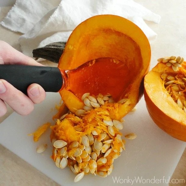 hand scooping seeds out of small pumpkin 