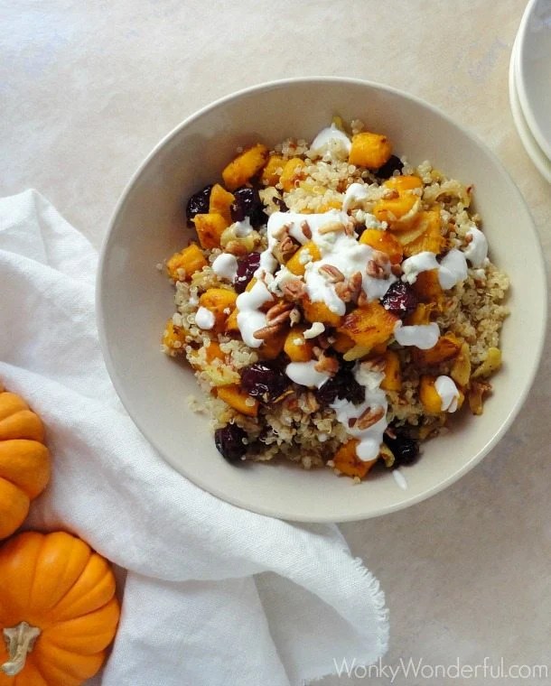 pumpkin quinoa in beige bowl next to plates and mini pumpkins