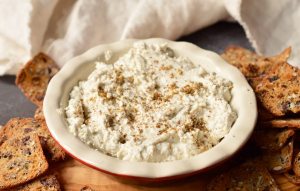 goat cheese dip in white and red serving dish with square crackers on the side