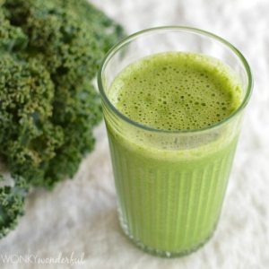 green frothy beverage in clear glass next to fresh kale