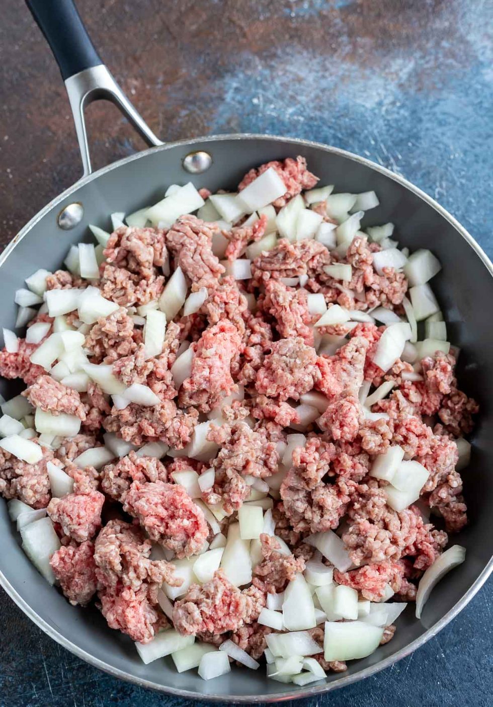 raw ground beef and chopped onions in fry pan