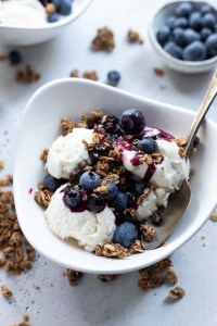 vanilla ice cream topped with blueberry sauce, berries and granola in white bowl