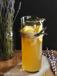 tan colored beverage and lemon slices in clear glass pitcher, lavender on the side