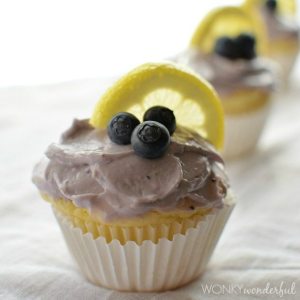 yellow muffin in white wrapper topped with frosting blueberries and lemon