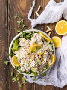 overhead photo of white bowl with chicken salad. lemons and micro greens around the bowl