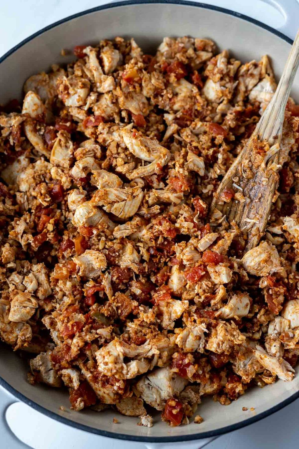 chicken, tomatoes and seasoning in pan with wooden spoon