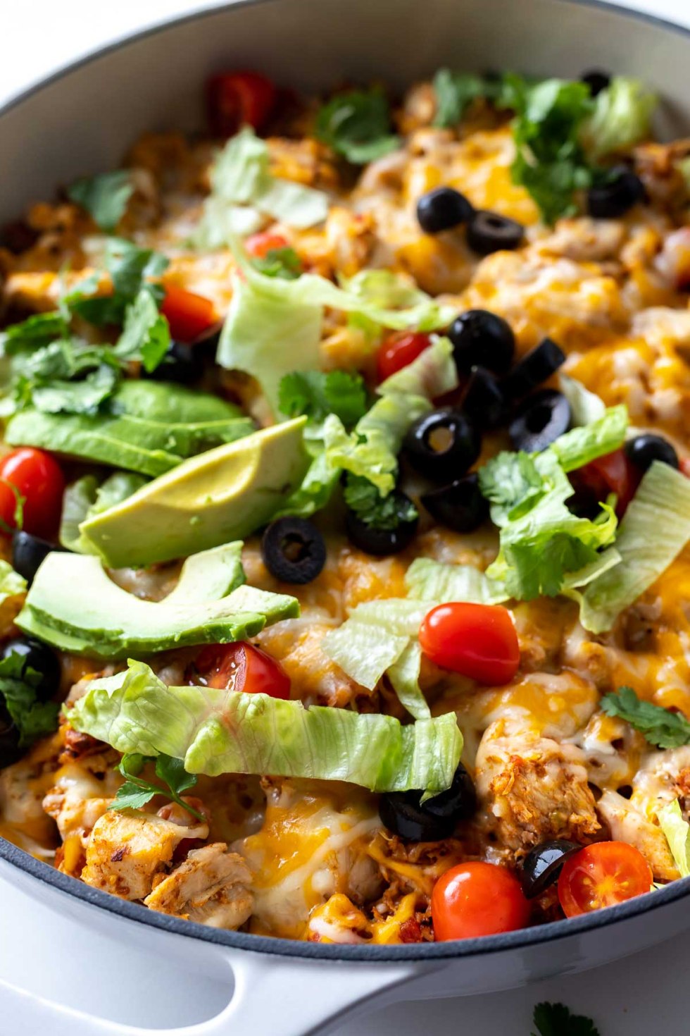 casserole topped with avocado, lettuce and olives in pan