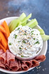 prepared dip in white bowl next to salami and veggies