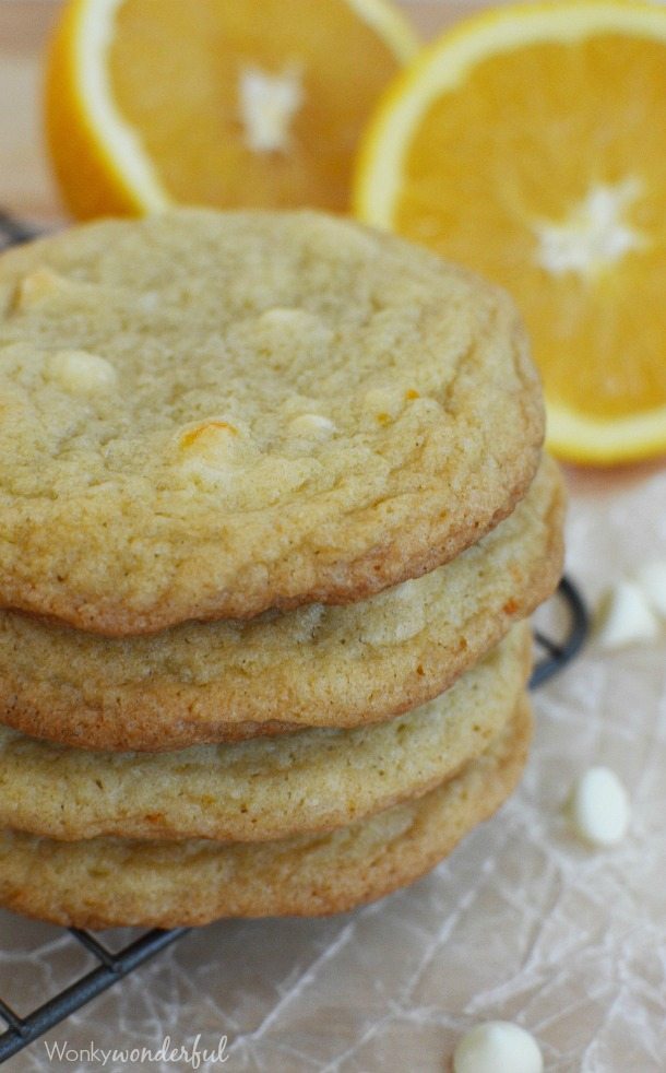 stack of light golden colored cookies with white chocolate chips and oranges in the background