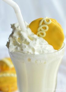 clear glass milkshake cup filled with creamy white shake and topped with whipped cream and an orange cupcake