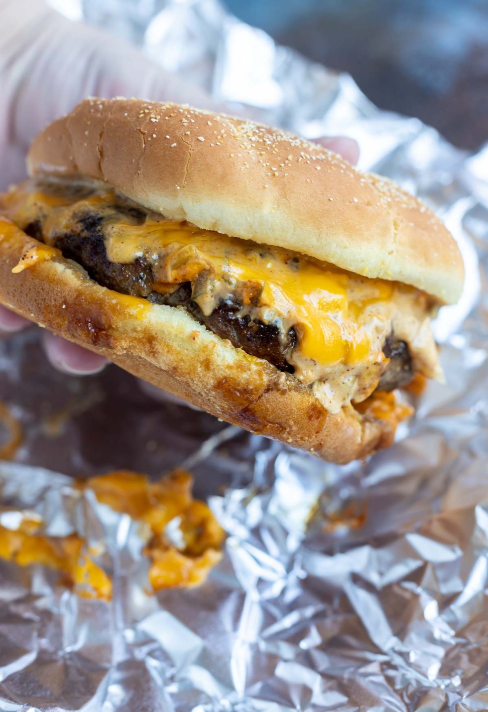 hand holding messy cheeseburger with melted cheese and sauce