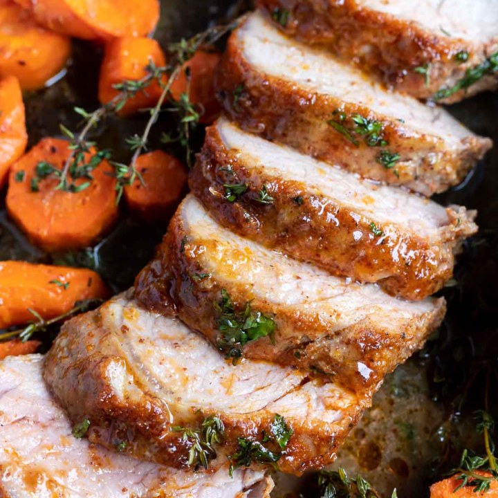 sliced cooked pork tenderloin and carrots on sheet pan