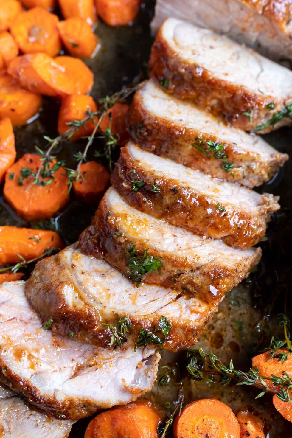 sliced cooked pork tenderloin and carrots on sheet pan