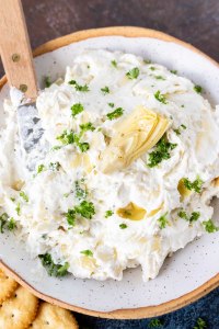 artichoke dip served in white bowl with spreading knife