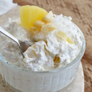 This Coconut Pineapple Fluff Recipe is light, airy and full of flavor! Coconut and Pineapple whipped with cream cheese and cool whip then topped with macadamia nuts. Serve straight from the bowl or as a dessert dip.