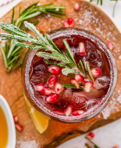 burgundy drink in glass topped with pom seeds and rosemary