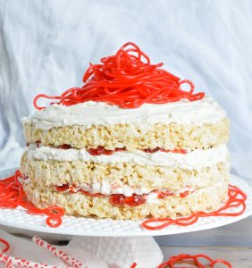 This Rice Crispy Treat Candy Cake is a fun and whimsical dessert recipe. Perfect for Valentine's Day, kids birthdays or for anyone that doesn't like traditional cake. Three layers of rice crispy treats smeared with vanilla butter cream, strawberry jam then topped with strawberry licorice ropes!