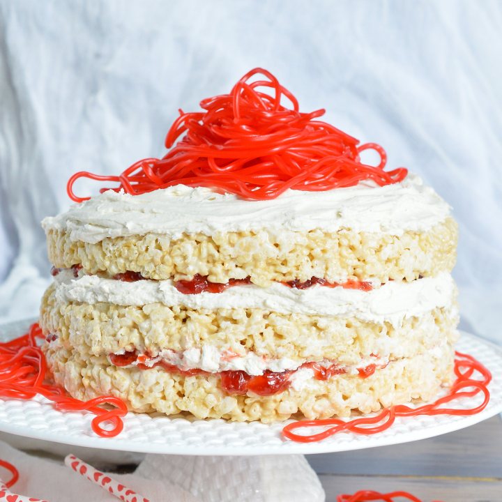 This Rice Crispy Treat Candy Cake is a fun and whimsical dessert recipe. Perfect for Valentine's Day, kids birthdays or for anyone that doesn't like traditional cake. Three layers of rice crispy treats smeared with vanilla butter cream, strawberry jam then topped with strawberry licorice ropes!