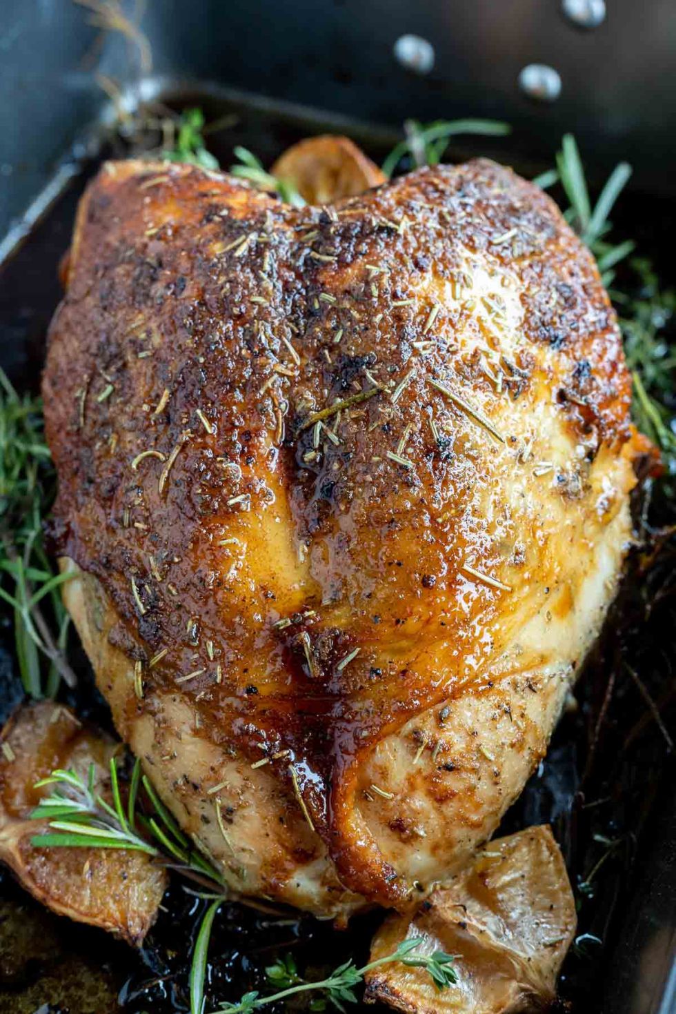 deep brown cooked turkey breast with herbs in roasting pan