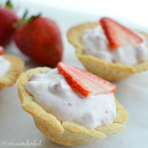 mini pie crust filled with pink mixture topped with sliced strawberry