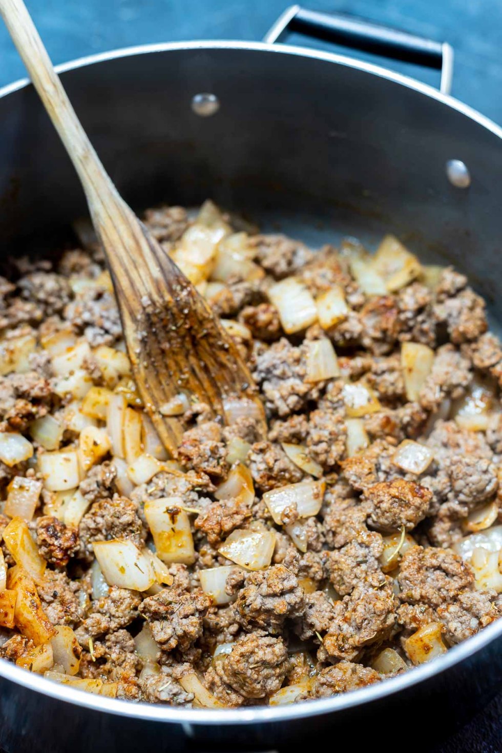 beef and onions with spices in pot with wooden spoon