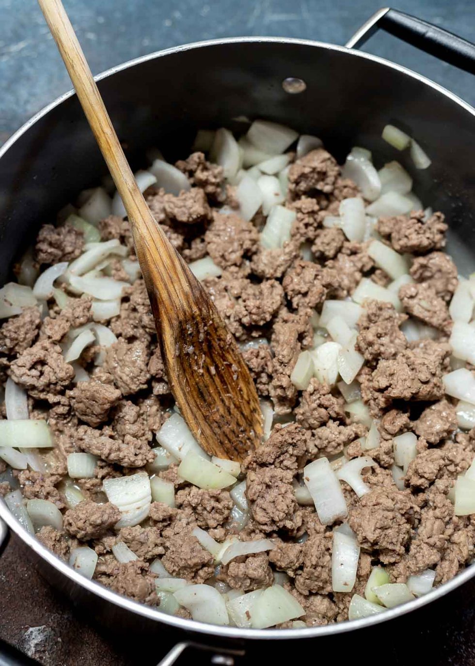 browned ground beef with chopped onions in pot with wooden spoon