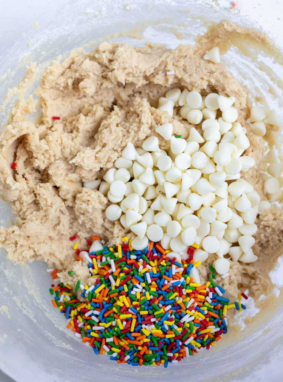 cookie batter, rainbow sprinkles and white chocolate chips in clear glass mixing bowl