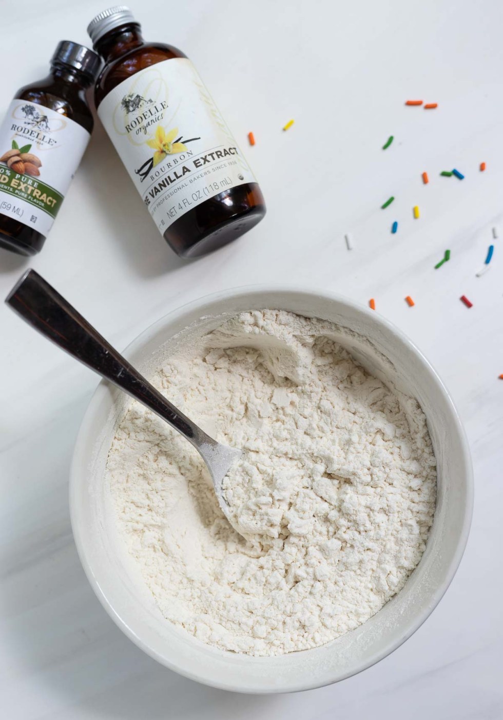 flour in bowl with spoon, flavor extract bottles on the side