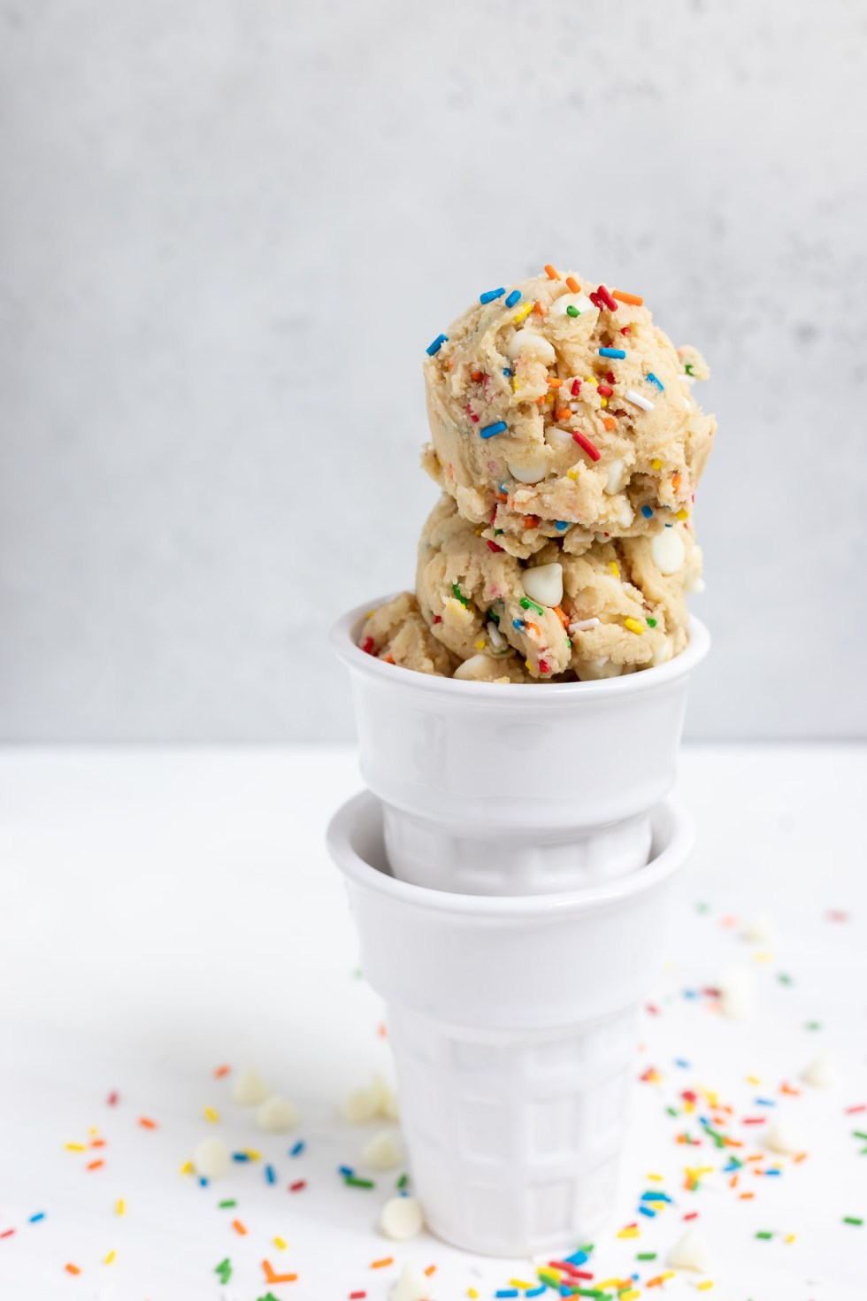 two glass dishes shaped like ice cream cones filled with cookie dough with sprinkles