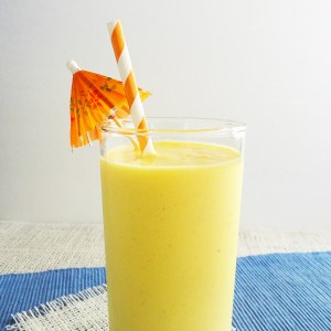 yellow smoothie in clear tall glass with straw and umbrella