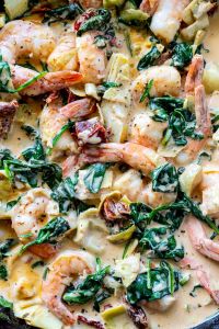 cooked shrimp in cream sauce with spinach, artichokes and dried tomatoes