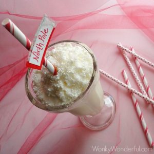 white milkshake in clear milkshake glass topped with whipped cream and a red and white striped straw with north pole sign attached